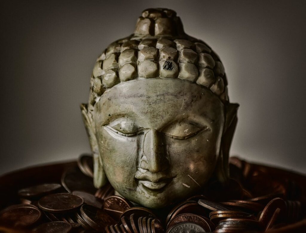 Close-up of Buddha head sculpture resting on bronze coins, symbolizing spirituality and prosperity.